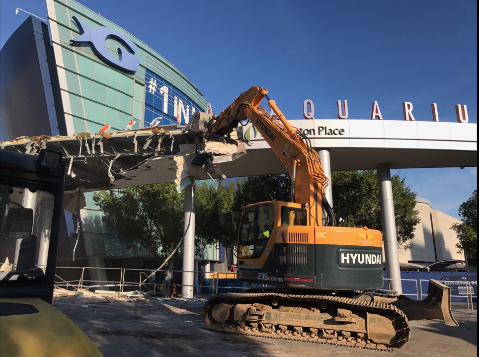 A yellow excavator demolishing a structure with an AQUARIUM sign