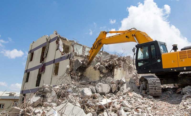 A yellow excavator demolishing a two-story building